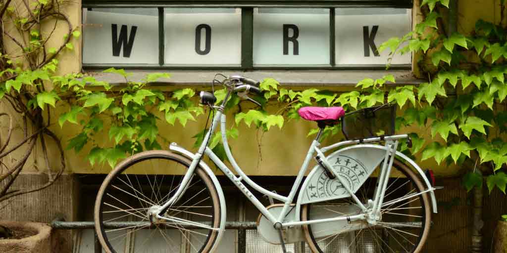 White bicycle parked beneath a WORK sign and climbing ivy