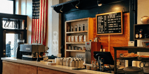 looking at a coffee shop counter, coffee machine, bags of coffee on shelves, and a menu hanging on the wall