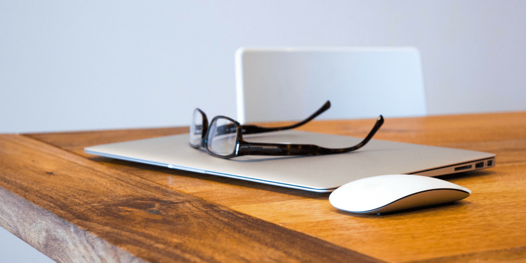 Closed laptop with eyeglasses and a mouse on a wooden desk