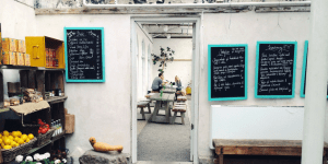 Image of the back of a store or restaurant, an open door to an outdoor patio with picnic tables and people eating. 