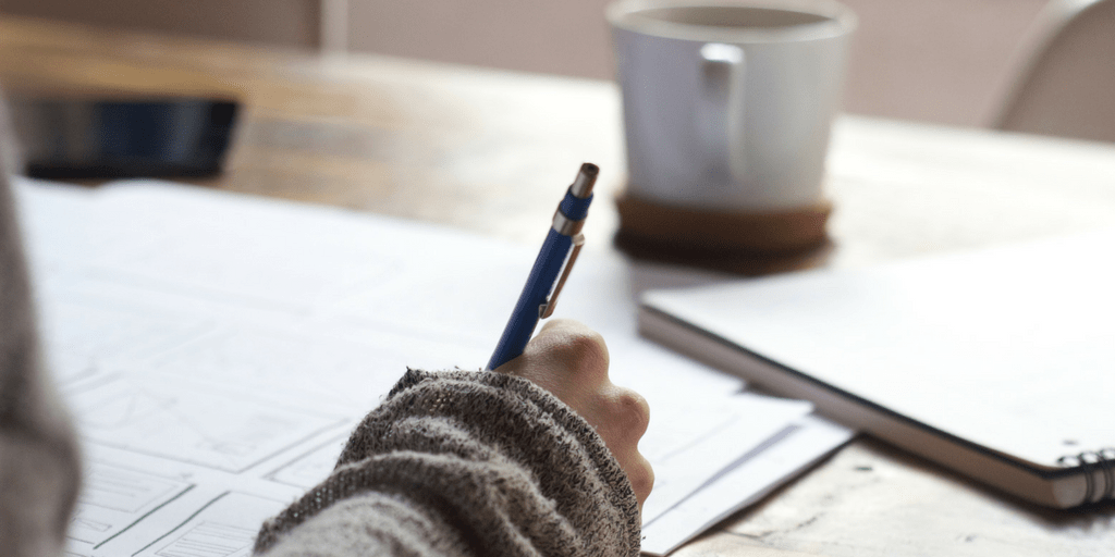 Hand writing notes on paper beside a coffee mug