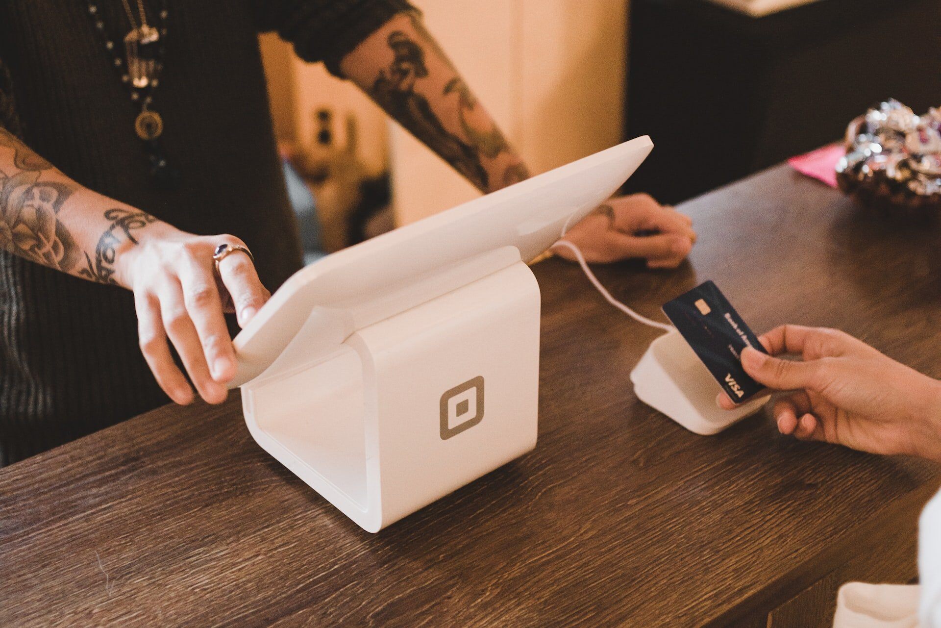 image of a closeup of 2 people at a counter, one at a modern cash register, the other holding a card paying. 