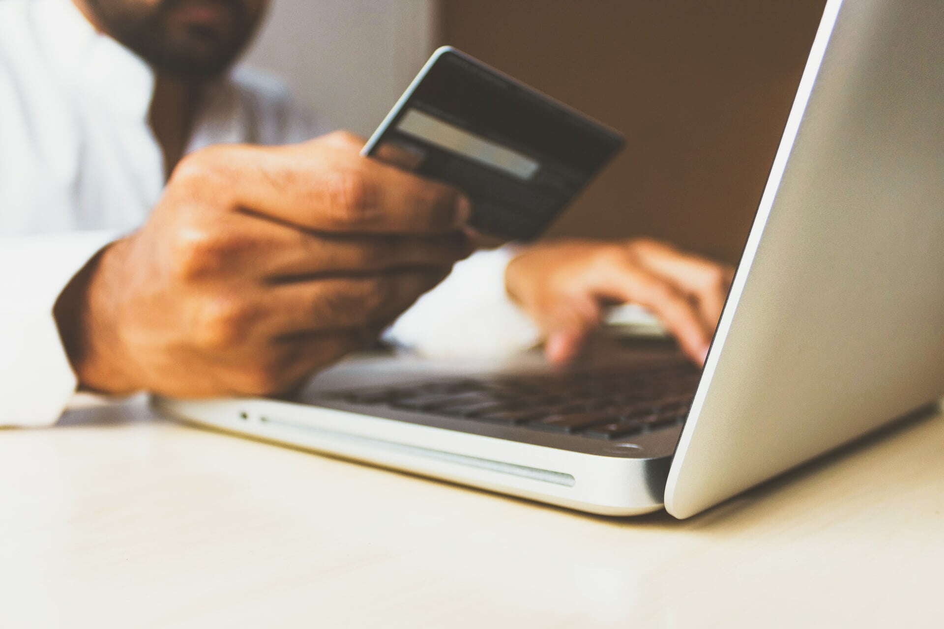 close up image of a man's hand, holding a credit card, and typing into his computer. 