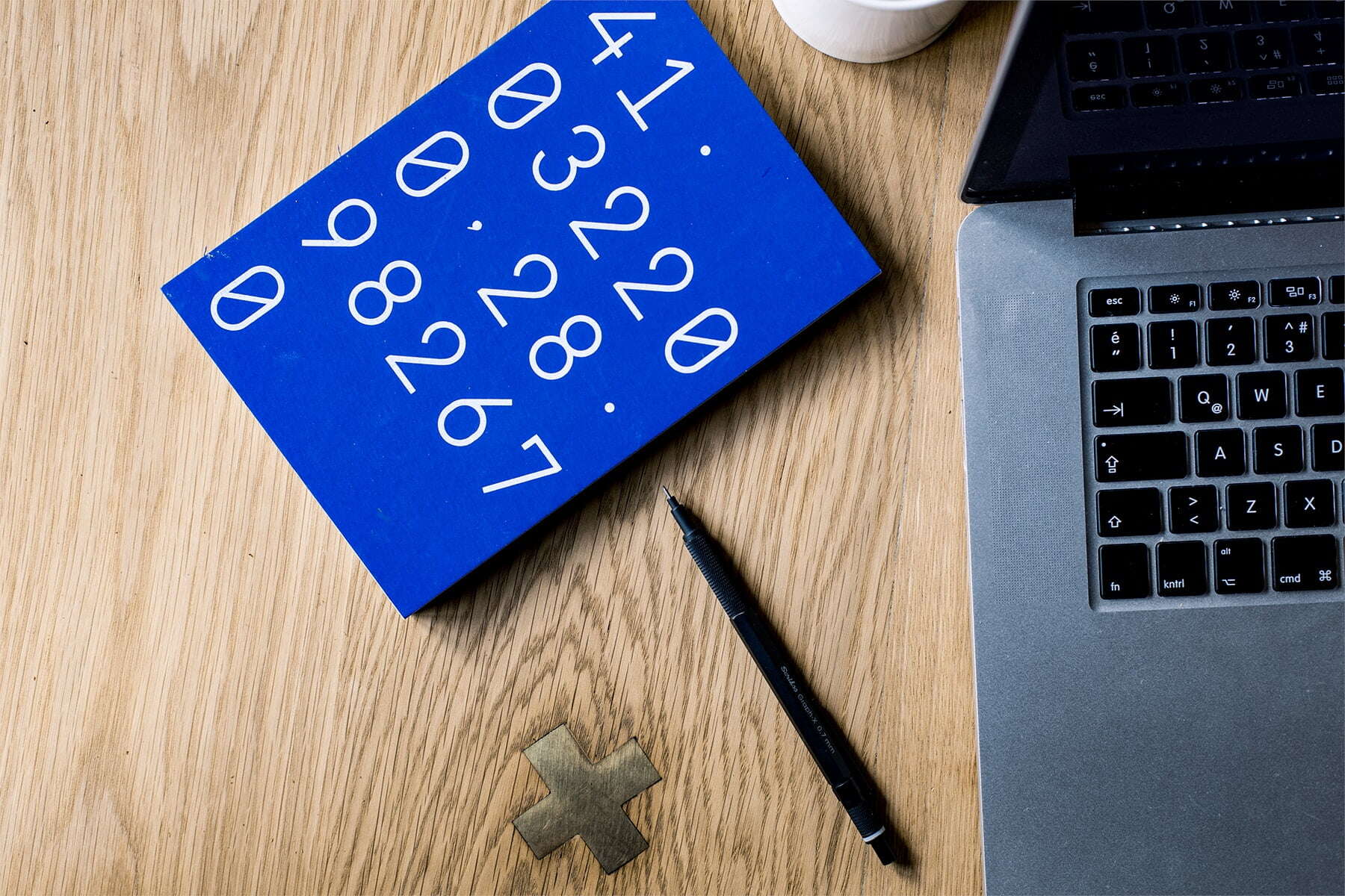 zoomed in image of a laptop, mechanical pencil, and a blue book that has numbers on it