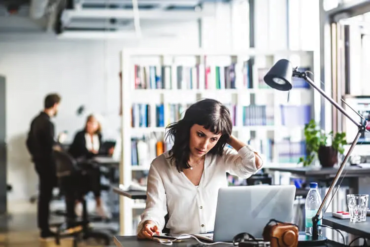 A woman in an office looking at a computer with a stressed out look on her face. 