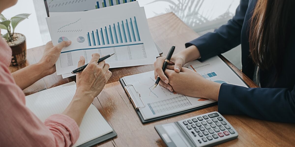 Two colleagues reviewing printed financial statements and charts at a desk with a calculator